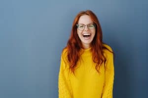 Young redhead woman with lovely sense of humor laughing uproariously at the camera over a blue studio background with copy space