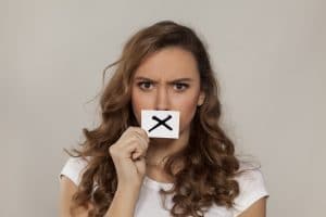 Concerned woman with X sign drawn on paper over her mouth