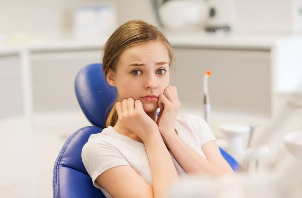 people, medicine, stomatology and phobia concept - scared and terrified patient girl at dental clinic office