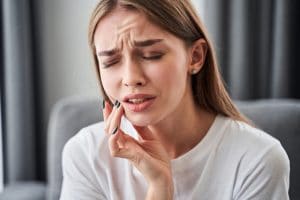 Can not take the pain. Frustrated young women suffering from toothache and touching her cheek with her fingers while sitting on the sofa at home