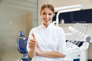Image of beautiful happy young woman doctor wearing white lab coat in medical dentist center showing thumb up