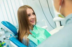 A beautiful girl is sitting in the dental chair and looking at a man doctor who is talking to her. dental clinic