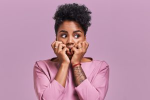 Emotions concept. Nervous emotional scared young lovely African American female stares at camera and opens mouth widely, notices phobia, expresses her fear against something, poses alone indoor.