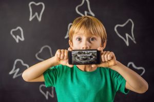 The boy shows his X-ray image of his teeth with an abnormally strange extra tooth. Children's dentistry. Patient Orthodontist.