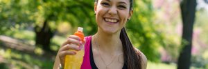 Smiling young woman holding energy drink outdoors in a park.