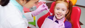 the child is a little red-haired girl smiling sitting in a dental chair. Pediatric dentistry, baby teeth