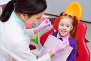the child is a little red-haired girl smiling sitting in a dental chair. Pediatric dentistry, baby teeth