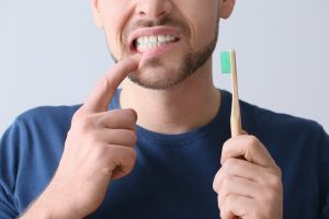 Man with aching teeth and brush on grey background