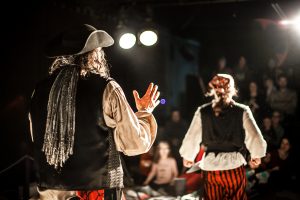 A creative shot with shallow depth of field from behind two performing arts entertainers dressed as pirates on a theater stage during comedy act.