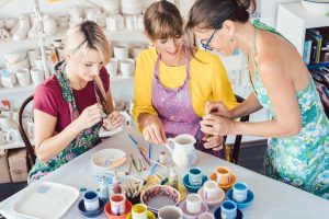 Teacher showing two women in workshop how to paint self-made dishes