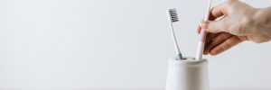 Hand takes a toothbrush from a white cup. One brush stands out. White background with copy space. oral care concept