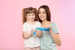 Little girl and her mother with mouthwash on color background. Teeth and oral care