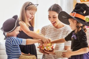 Happy family celebrating Halloween! Young mom treats children with candy. Funny kids in carnival costumes.