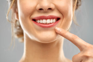 oral care, dental hygiene and people concept - close up of finger pointing to woman face with healthy white teeth over gray background