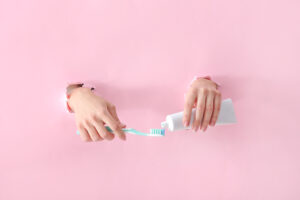 Female hands with toothbrush and paste on color background