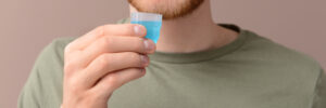 Young man with cup of mouthwash on color background
