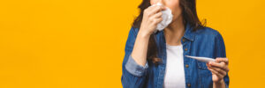 Young woman having flue taking thermometer. Isolated against yellow background. Beautiful young woman is sick with a high temperature, a thermometer, isolated close-up. Cold, flu concept.