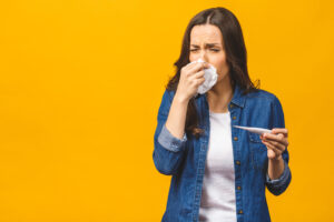 Young woman having flue taking thermometer. Isolated against yellow background. Beautiful young woman is sick with a high temperature, a thermometer, isolated close-up. Cold, flu concept.