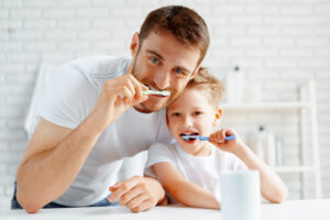 Dad and little son brushing teeth together in bathroom