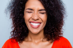 Closeup cropped portrait of funny comic woman with clenched white healthy teeth close eyes making a wish isolated on grey background. Toothcare tooth care treatment therapy concept
