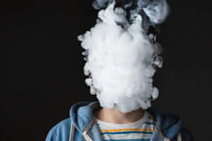 The face of vaping young man on black studio background
