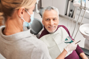 New smile. Back view of the female blonde caucasian doctor presenting dental impression for dentures to the senior smiling man. Stock photo