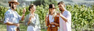 Group of young friends dressed casually having fun together, tasting wine on the vineyard on a sunny summer morning