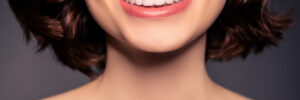 Cropped photo of smiling cheerful female naked shoulders showing perfect teeth after treatment isolated on black color background
