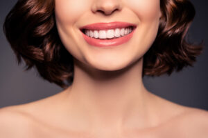 Cropped photo of smiling cheerful female naked shoulders showing perfect teeth after treatment isolated on black color background