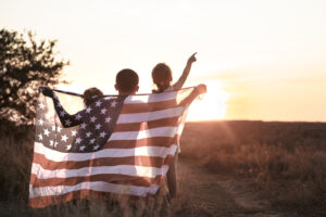 Happy family, dad and daughter holding the American flag at sunset. Dressed in white. The concept of family values and friendship . Patriotic feeling.