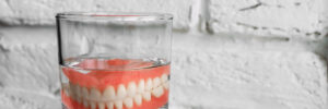 A denture in a glass of water. Dental prosthesis care. Full removable plastic denture of the jaws. Two acrylic dentures. Upper and lower jaws with fake teeth. Dentures or false teeth, close-up.