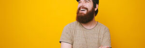 Portrait of cheerful bearded man smiling and looking away over yellow background