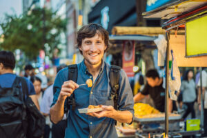 Young man tourist eating Typical Korean street food on a walking street of Seoul. Spicy fast food simply found at local Korean martket, Soul Korea.