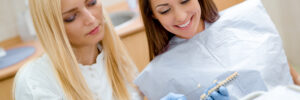 Beautiful young smiling woman at visit in the dentist office and female dentist showing her porcelain crowns.