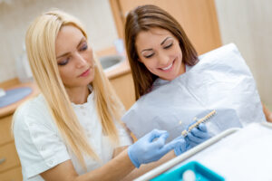 Beautiful young smiling woman at visit in the dentist office and female dentist showing her porcelain crowns.