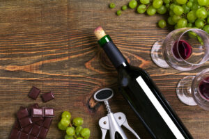 Red wine bottle, grape, chocolate and glasses over wooden table. Top view with copy space. Still life. Flat lay