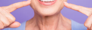 Concept of having strong healthy straight white perfect teeth at old age. Cropped portrait of beaming smile female pensioner pointing on her teeth, isolated over violet background