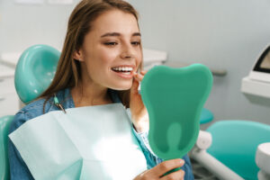 European young woman smiling while looking at mirror in dental clinic