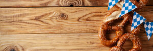 Oktoberfest concept with pretzel and blue simbol flag on wood background, copy space, top view, flat lay, border