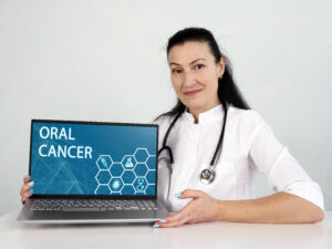 ORAL CANCER inscription on the screen. Close up Neurologist hands holding black laptop.