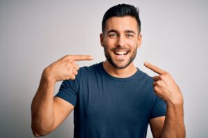 Young handsome man wearing casual t-shirt standing over isolated white background smiling cheerful showing and pointing with fingers teeth and mouth. Dental health concept.