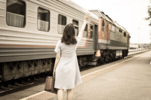 Young woman in with a suitcase waves to the departing train. Ret